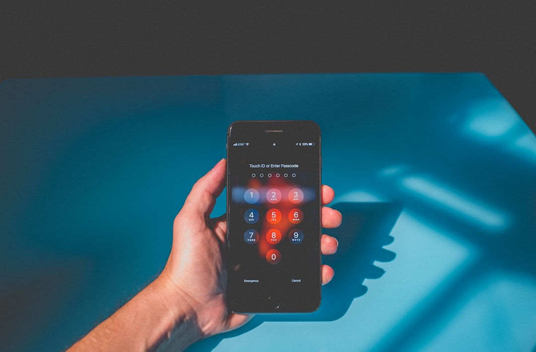 A hand holding a smartphone at a passcode entry screen, illustrating the two-factor authentication step attackers targeted via 2FA backup codes