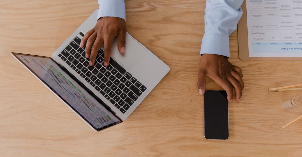 Hands on a laptop and phone at a desk during a phishing simulation testing exercise