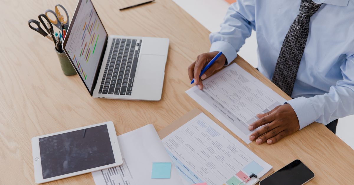 A hand reviewing a printed patch priority checklist alongside a laptop on an office desk