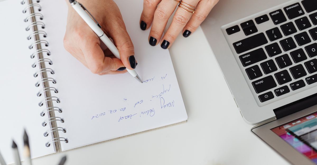 A hand writes a security checklist note next to a MacBook, a practical step against the Atomic macOS Stealer