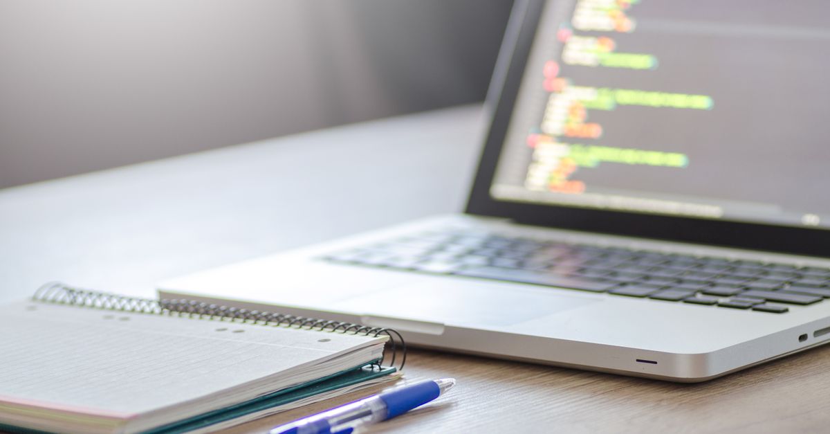 An open laptop showing lines of code next to a notebook, illustrating a vulnerability management review in progress