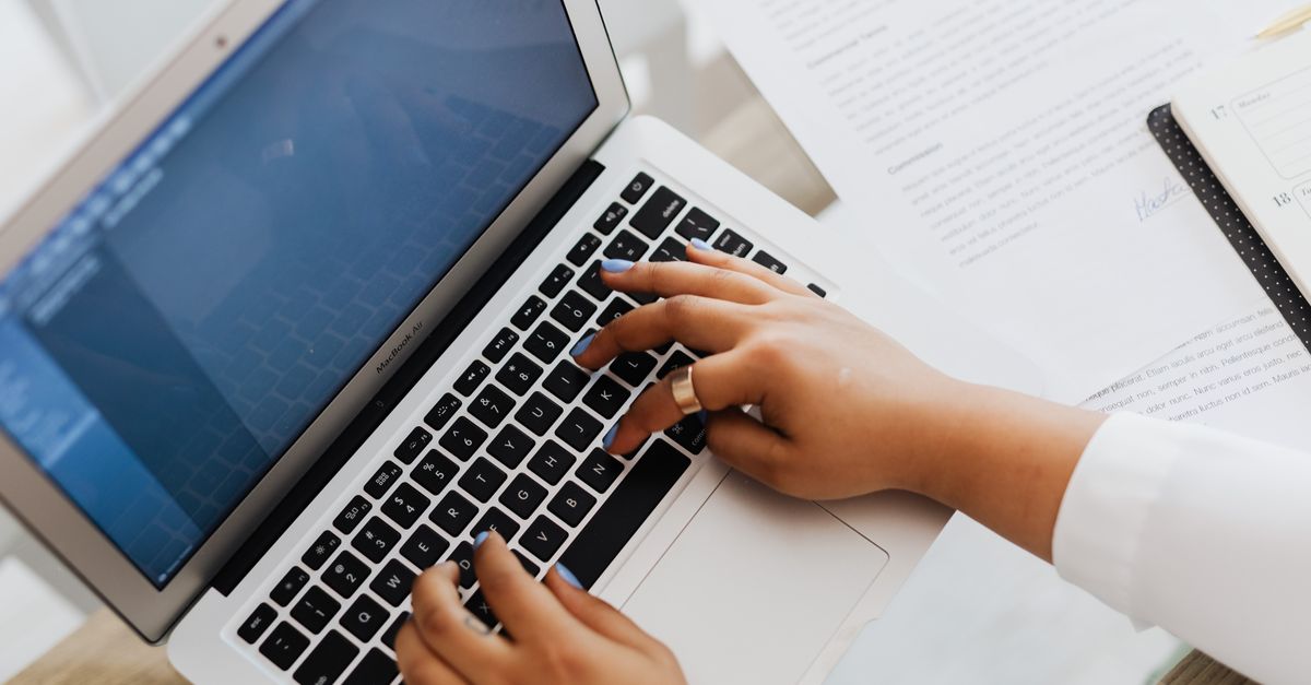 Hands typing on a laptop next to printed documents, showing how DLL sideloading attacks start with an ordinary-looking file