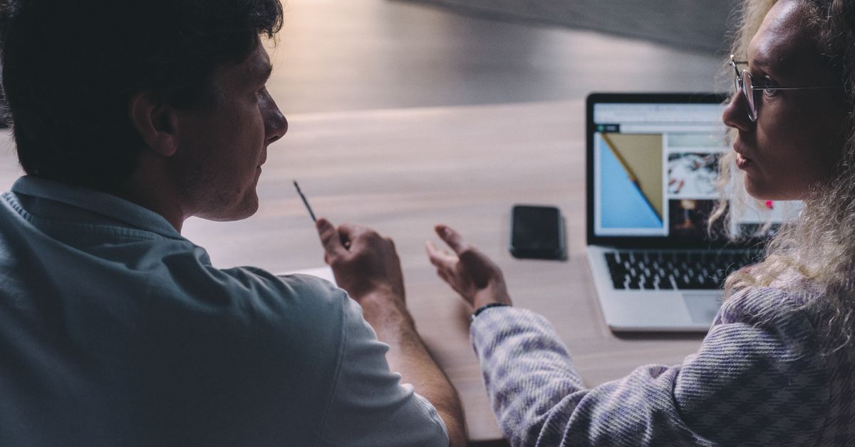 Two colleagues discussing a supplier's paperwork and laptop during a procurement meeting