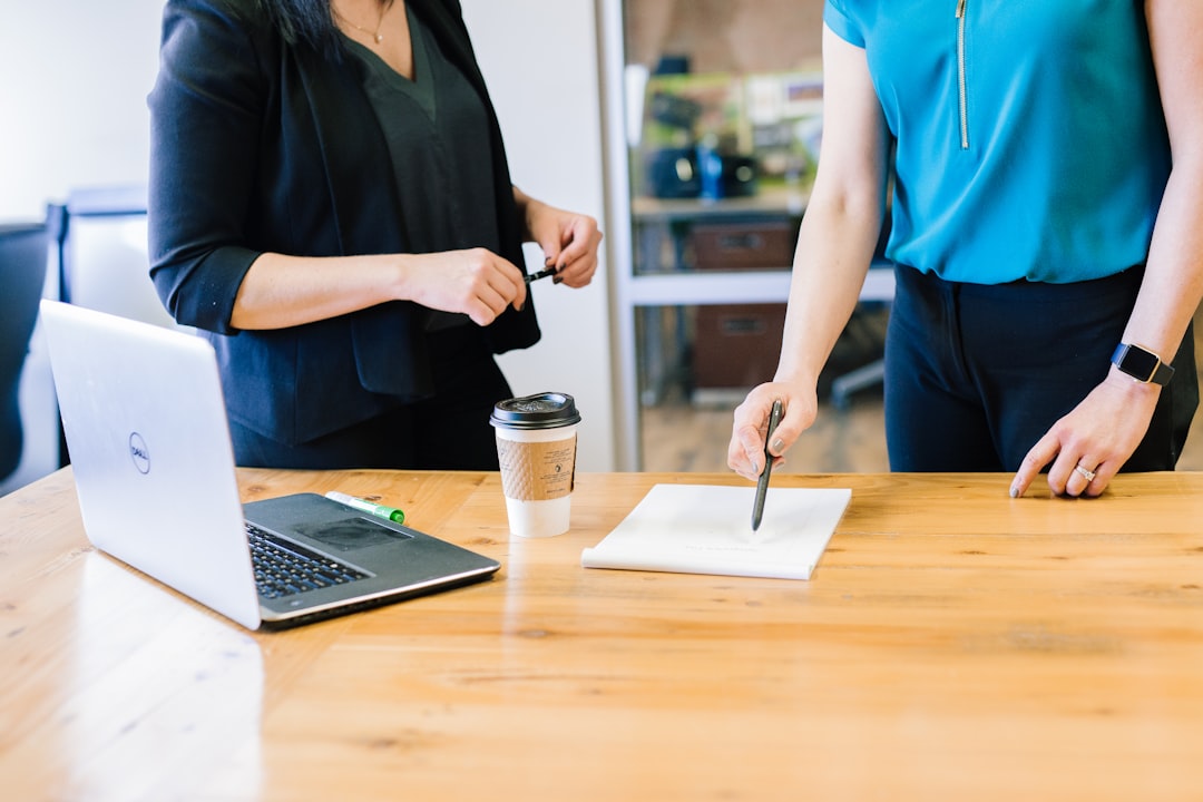 Two colleagues reviewing documents at a table with a laptop, representing the on-premises SharePoint systems affected by the authentication bypass
