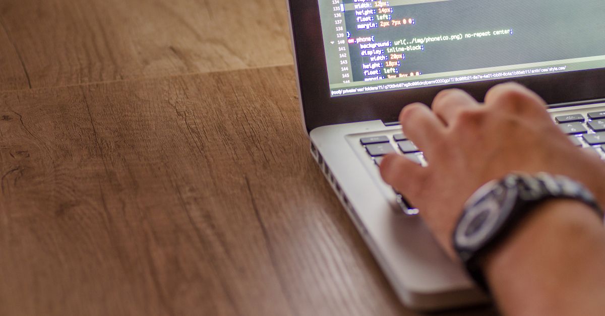A hand on a laptop keyboard with website source code on screen, checking for third party plugin risk
