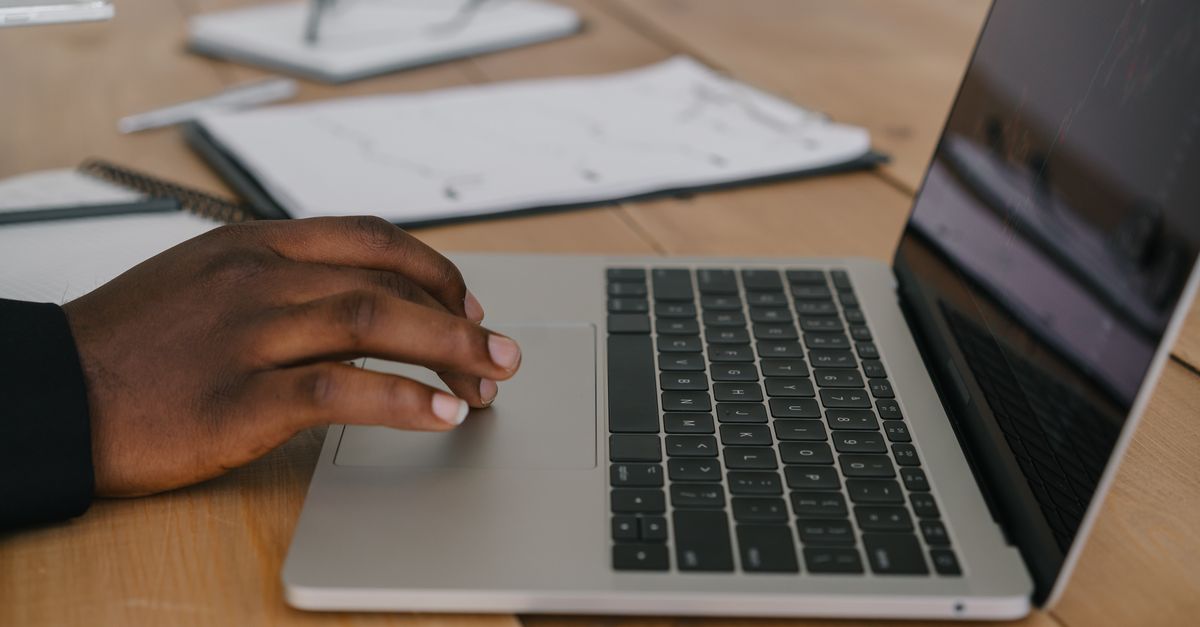 A hand on a laptop trackpad next to paperwork, the everyday sign-in moment device code phishing targets