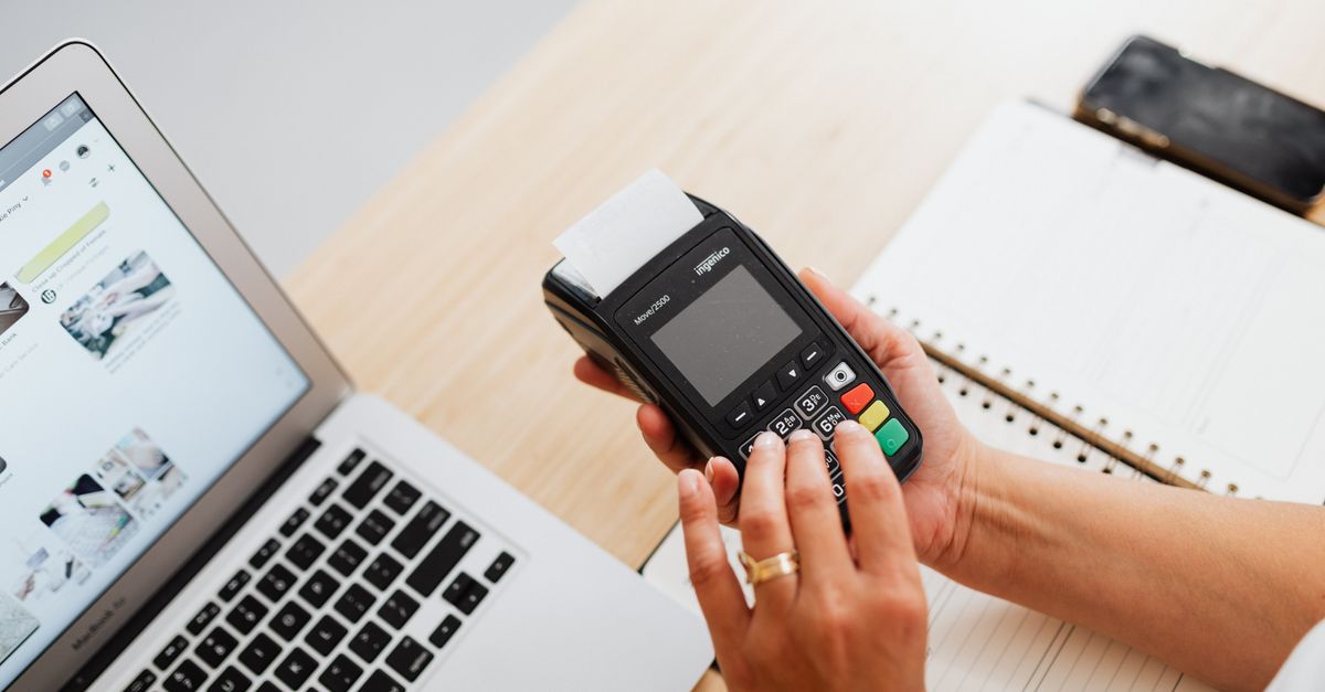 A payment card terminal beside a laptop, representing the verification step that stops a business email compromise payment going through