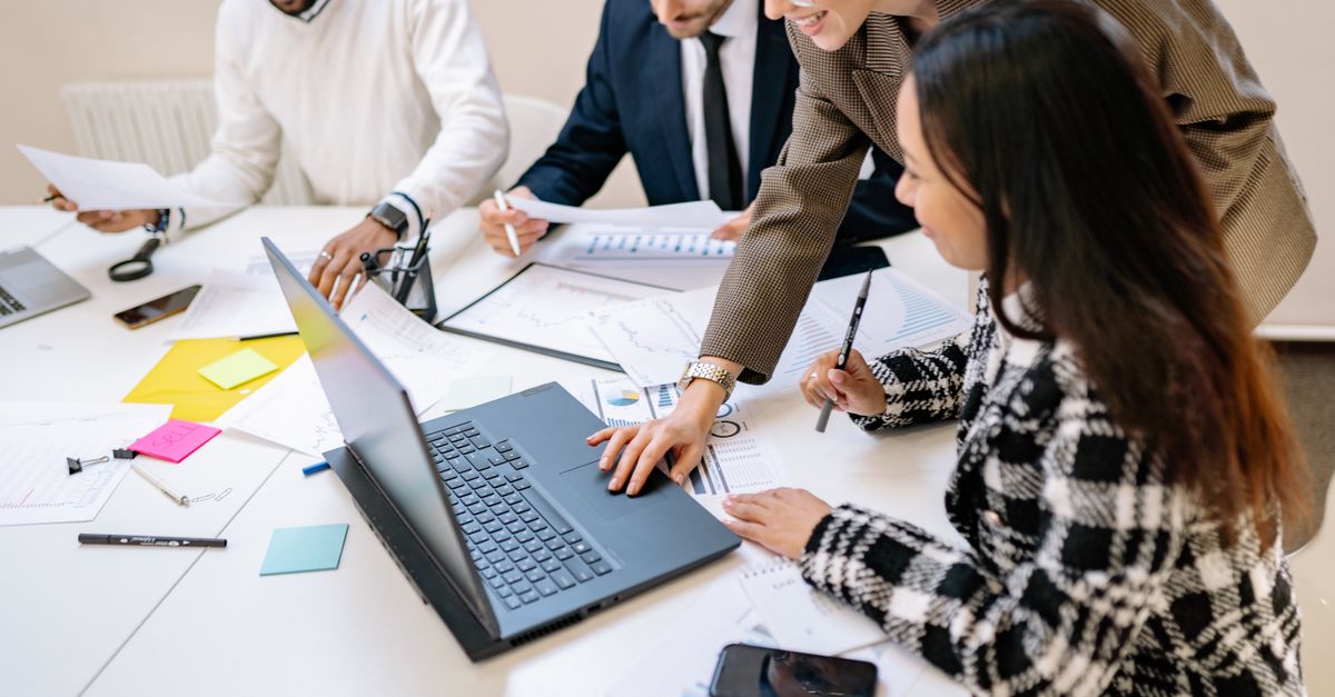 A small business team gathered around a laptop reviewing documents together in the office