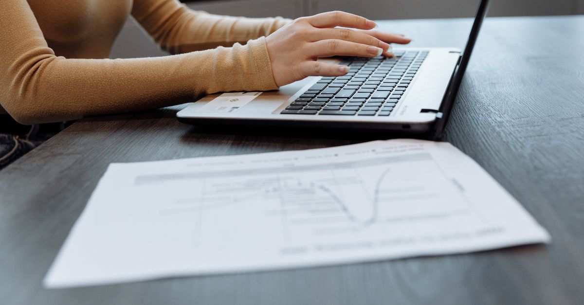 Hands typing on a laptop next to a printed report, reviewing a zero-day vulnerability advisory