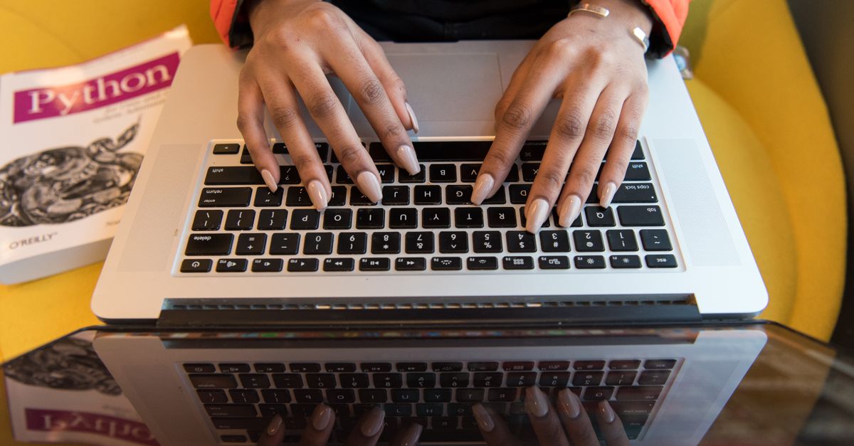 Hands typing on a laptop next to a programming book, reflecting the AI coding assistant abused in the Aurora intrusions