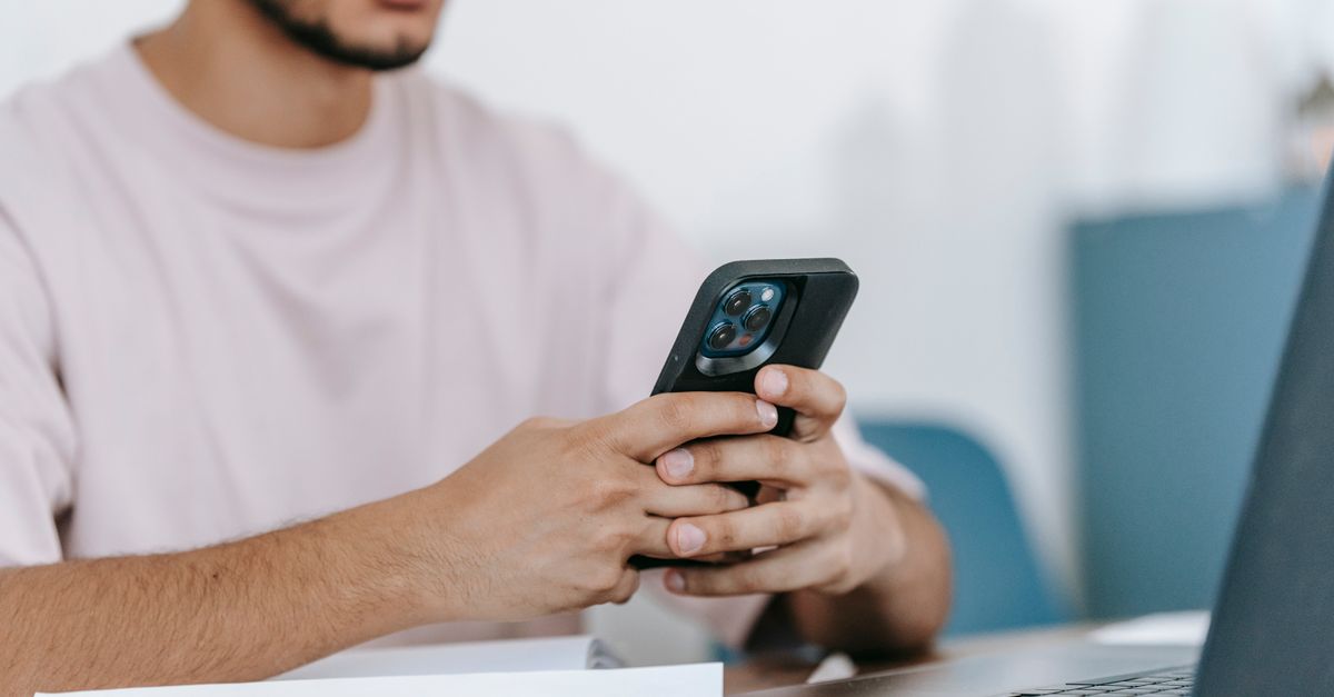 man checking his phone at an office desk next to a laptop
