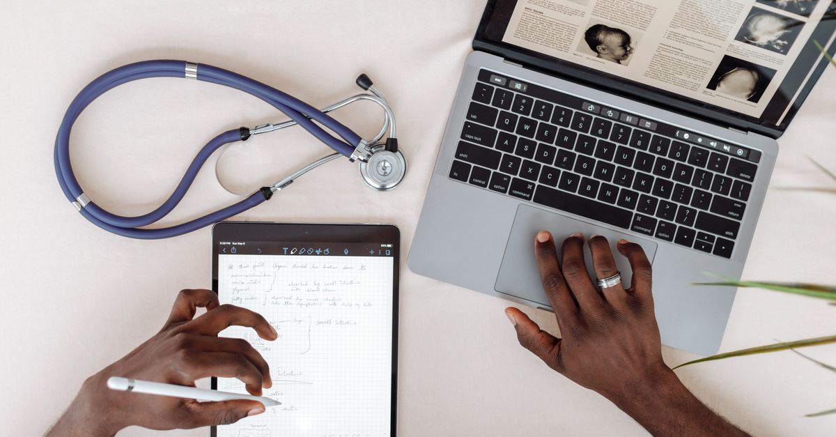 Doctor's hands on a laptop and tablet beside a stethoscope, where penetration testing for healthcare protects patient data
