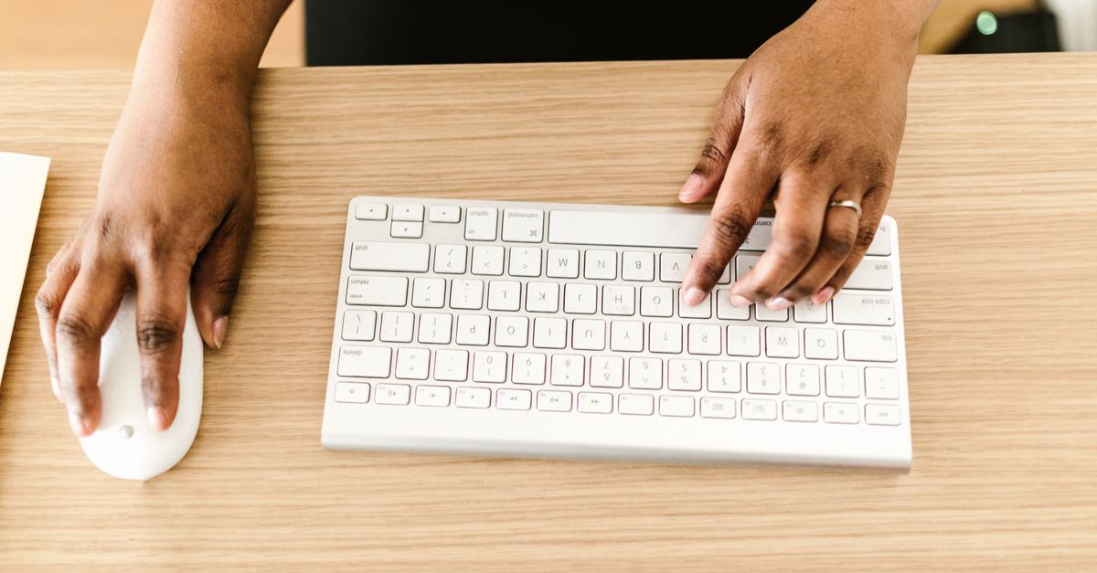 Hand on a computer mouse at a workstation, the kind of low-rights account a privilege escalation attack starts from