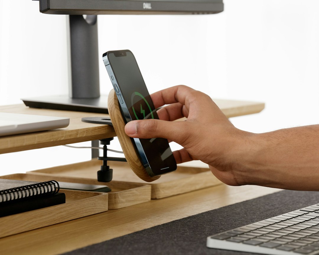Hand placing a phone on a desk stand, the kind of work iPhone the DarkSword exploit kit targets